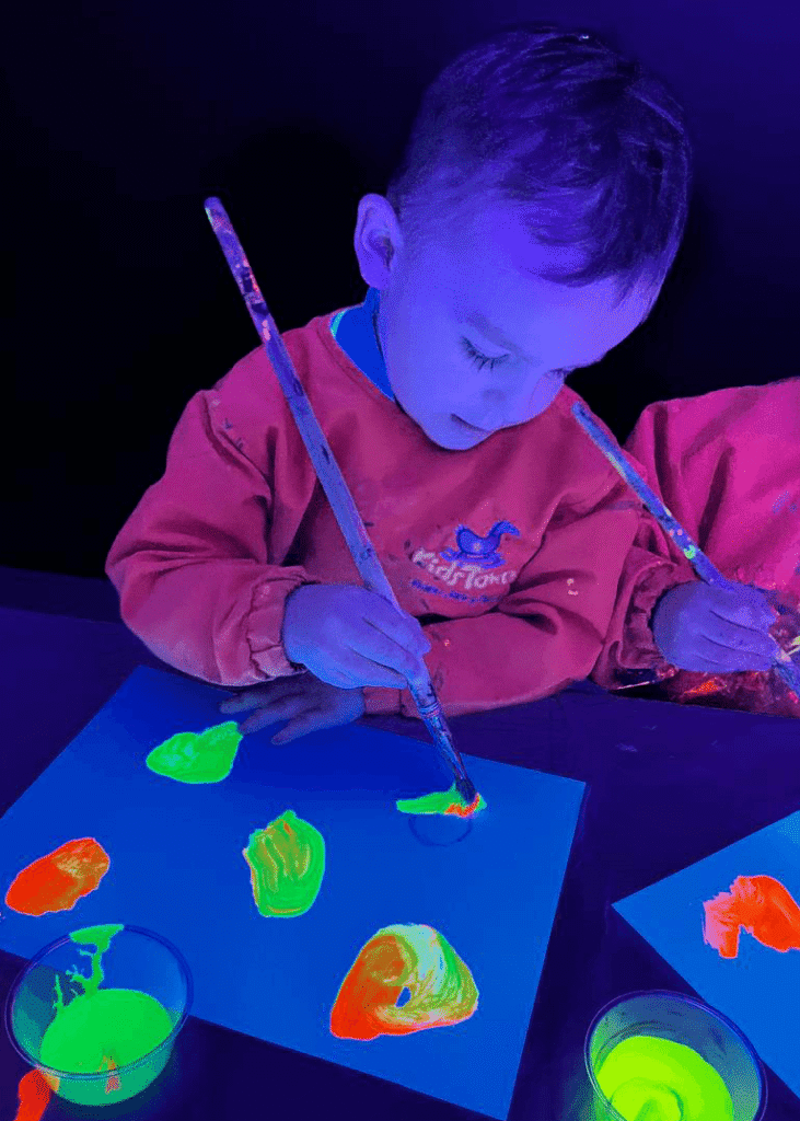 Niño realizando actividad artística con pintura fluorescente en Kids Town